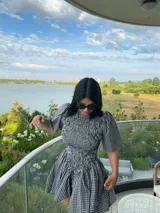 Vestido corto con estampado de cuadros vichy en blanco y negro. Presenta un cuerpo ajustado con efecto fruncido, mangas cortas abullonadas y falda con vuelo.