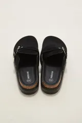 Suecos negros de estilo casual con acabado en eco cuero, detalle de hebilla metálica ajustable en el empeine y tachas decorativas en el contorno de la suela. Presentan una base de corcho y suela de goma dentada.
