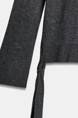 Jersey de punto liso color gris oscuro, con cuello redondo, manga larga y detalle de tiras largas en los laterales del ruedo.