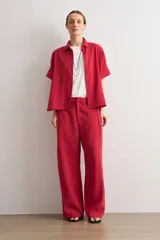 Pantalón de corte recto y pinzas delanteras, color rojo, con bolsillos laterales y cierre frontal con botón y cremallera.