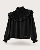 Blusa negra de manga larga con cuello alto y detalle de nido de abeja (smock) en el pecho y hombros, decorado con volados. Presenta puños elásticos con volados y una pequeña etiqueta de cuero con el logo de la marca en el ruedo.