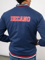 Campera bomber azul marino estilo retro, con cierre frontal de botones a presión, cuello, puños y ruedo con tejido acanalado tricolor. Presenta el logo de Umbro y el escudo del Club Nacional de Football bordados en el pecho, junto con el año 1899 y parches decorativos en las mangas.