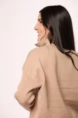 Buzo tejido de punto color beige, con cuello alto y cierre frontal parcial. Presenta mangas largas con diseño en tejido morley y corte holgado.