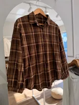 Camisa de manga larga con diseño de cuadros en tonos marrones y beige. Presenta cuello clásico, cierre frontal con botones y mangas con puños fruncidos.