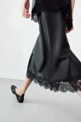 Falda midi de tiro alto confeccionada en tejido efecto piel color negro. Presenta un diseño de corte recto con bajo acabado en aplicación de encaje a tono y abertura en la espalda. Cierre mediante cremallera oculta en la costura posterior.