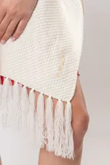 Ruana de tejido en color crudo, de diseño abierto con flecos en el ruedo inferior y detalles bordados.