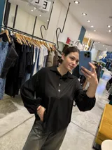 Blusa negra de manga larga abullonada con puños elásticos, cuello camisero y cierre frontal parcial de botones metálicos dorados.