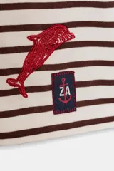 Camiseta de manga larga con cuello redondo y rayas horizontales marrones y blancas. Presenta bordados de temática marina en rojo (caballito de mar y delfín), un símbolo de porcentaje (%) bordado en marrón en el pecho y una etiqueta con texto en la manga.