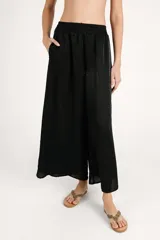 Pantalón fluido de corte ancho, color negro con sutil acabado brillante, cintura elástica y diseño holgado.