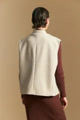 Chaleco de paño color marrón oscuro, de silueta recta y diseño minimalista. Presenta cuello a la base, cierre frontal con botones claros y bolsillos aplicados.