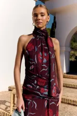 Vestido midi bordó de Lady Pipa, con estampado floral en tonos rojos y celestes, cuello halter fruncido, diseño sin mangas con espalda descubierta y detalle fruncido en la cintura y cadera.