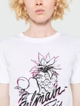 Remera de algodón blanca con cuello redondo y manga corta. Presenta un estampado frontal con diseño de piña y frutas, acompañado por el logo de Balmain Paris en tipografía cursiva con detalles en color rosado.
