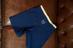 Calza corta deportiva color azul marino, tiro alto, con pretina ancha de color amarillo claro y un pequeño logo bordado en la parte trasera central superior.