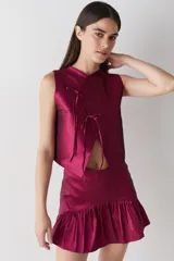 Top sin mangas de estilo cruzado, confeccionado en tela satinada color cobre. Presenta un diseño corto con cierre frontal mediante tiras finas para anudar y cuello redondo.