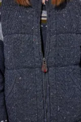 Chaleco tejido de punto color marrón con cuello de piel sintética, cierre frontal con cursor de cuero y diseño acolchado con cortes horizontales.