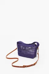 Bolso de mano tejido color violeta con asa corta y correa de cuero marrón extraíble.