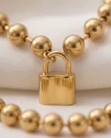 Pulsera de acero italiano con baño de oro, compuesta por una cadena de eslabones tipo bolitas y un dije central en forma de candado.