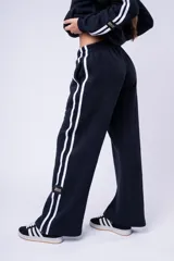 Pantalón de jogging color marrón, de corte recto y holgado, con cintura elástica y doble franja lateral blanca. Presenta una etiqueta pequeña con la marca en la parte inferior de la pierna.
