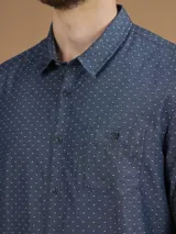 Camisa de manga larga azul con pequeños lunares blancos, cuello clásico y bolsillo en el pecho.