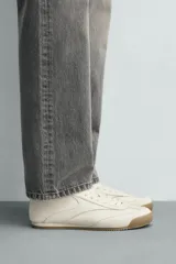 Zapatilla de estilo retro con cordones, confeccionada en una combinación de piezas de cuero sintético negro y detalles en blanco, con suela dentada de goma en tono caramelo.