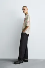 Camiseta de punto de algodón con corte boxy fit, cuello redondo y manga corta. Presenta un estampado frontal con temática de taller mecánico en tonos rojo desgastado y negro, incluyendo el texto "Rust & Revive", "Old Iron Garage" y detalles técnicos. La prenda tiene un efecto lavado y acabados irregulares.