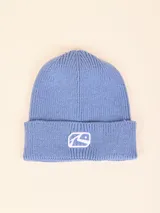 Gorro tipo beanie de tejido de punto acanalado en color azul, con vuelta y parche bordado con el logo de la marca en el frente.