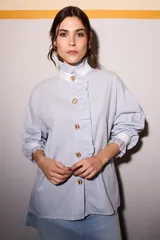 Camisa celeste a rayas verticales azules y marrones, con cuello blanco, cierre frontal con botones dorados y volantes verticales.