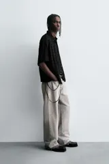 Camisa negra de corte relajado con tejido semitransparente de estructura abierta y patrón a cuadros. Presenta cuello solapa, manga corta, bolsillo plastrón en el pecho y cierre frontal de botones.