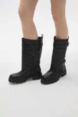 Bota de caña media en color negro, confeccionada en eco cuero con suela track dentada. Presenta un diseño con doble tira ajustable con hebillas metálicas en el lateral externo.