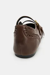 Zapato plano tipo bailarina de piel en color marrón, con detalles de perforaciones estilo brogue, doble tira delantera con hebillas metálicas doradas y puntera cuadrada.