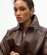 Campera de cuero sintético color marrón oscuro, con cuello clásico, cierre frontal metálico, dos bolsillos frontales amplios con solapa y ruedo con elástico.