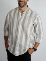 Camisa de manga larga con cuello mao, confeccionada en tela a rayas verticales en tonos blanco y beige. Presenta cierre frontal con botones y logo bordado en el pecho.