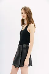 Falda corta negra de cuero ovino con diseño cruzado tipo wrap. Presenta apliques de tachas y piedras plateadas y doradas a lo largo de los bordes y en la cintura.