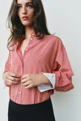 Camisa de cuello solapa y manga larga con rayas verticales rojas y blancas, con puños anchos blancos contrastantes y cierre frontal de botones.
