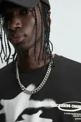 Camiseta negra de corte relaxed fit, cuello redondo y manga corta. Presenta un estampado frontal en blanco con efecto spray que simula dos figuras volando, y texto en un óvalo que dice "SUCCESS CHASER".