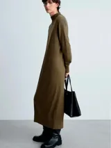 Vestido midi de punto fino en color verde oliva, con cuello alto tipo perkins, manga larga y diseño recto. Presenta un detalle de lazo anudado en la cintura y terminaciones en canalé.