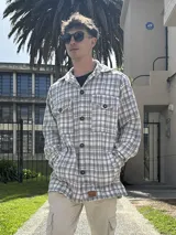 Sobrecamisa gris y blanca a cuadros con cuello camisero, cierre frontal con botones, bolsillos de parche en el pecho y bolsillos laterales.