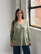 Sweater de punto color verde, con escote en V, mangas largas con puños acanalados y dos bolsillos frontales. Presenta una costura vertical central decorativa.