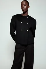 Chaqueta de corte recto confeccionada en mezcla de lana, con cuello redondo y manga larga. Presenta un diseño cruzado con botones metálicos plateados y acabados deshilachados en cuello, puños y ruedo.