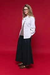Camisa blanca de manga larga con volumen y estructura, cierre frontal con botones y lazo ajustable en la cintura que realza la silueta.