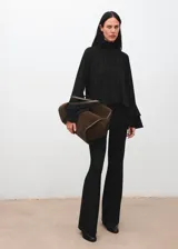 Blusa negra de cuello alto con cierre de botones, diseño recto y mangas largas acampanadas con volantes en los puños. Confeccionada en tejido fluido.
