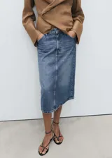 Falda midi de tiro medio confeccionada en tejido de algodón estilo denim. Presenta diseño evasé, cierre frontal con cremallera y botón, trabillas para cinturón y cinco bolsillos clásicos.