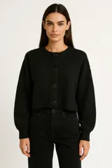 Cardigan de punto color negro, con cuello redondo, cierre frontal de botones y mangas largas con puños acanalados. Presenta un corte holgado y corto.