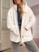 Campera de corderito blanco con capucha, de corte holgado y diseño tipo collage en la espalda con parches geométricos en tonos gris, negro y detalles en color. Incluye etiqueta de marca en la parte inferior trasera.