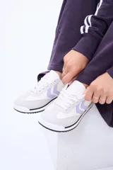 Championes urbanos de diseño moderno, combinan paneles en color blanco y gris claro con detalles en lila en los laterales. Presentan suela plana con una fina línea negra y cordones al tono.