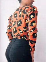 Remera manga larga color naranja con estampado animal print negro y dorado, con nudo en la parte delantera.