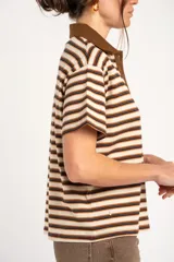 Remera polo de manga corta con diseño a rayas horizontales en tonos marrones, beige y negros, cuello en contraste y cierre frontal de botones.