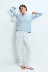 Pijama compuesto por una remera de manga larga en color celeste con textura acanalada y cierre frontal con botones, y un pantalón largo de corte recto en color blanco con rayas verticales celestes y cintura elástica con cordón ajustable.