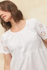 Vestido corto negro con escote redondo, mangas cortas con detalle de calado y falda escalonada con detalle de calado en el ruedo.