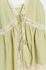 Top lencero de viscosa color verde menta, con tirantes finos, escote en V y detalles de encaje color crema en el escote, cintura y ruedo. Presenta cierre frontal con lazos ajustables.